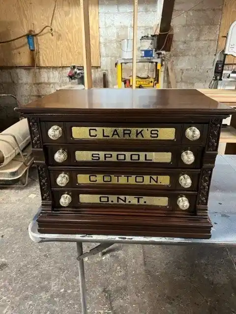 The same spool cotton cabinet after refinishing, glossy with its brass-framed drawer labels clear