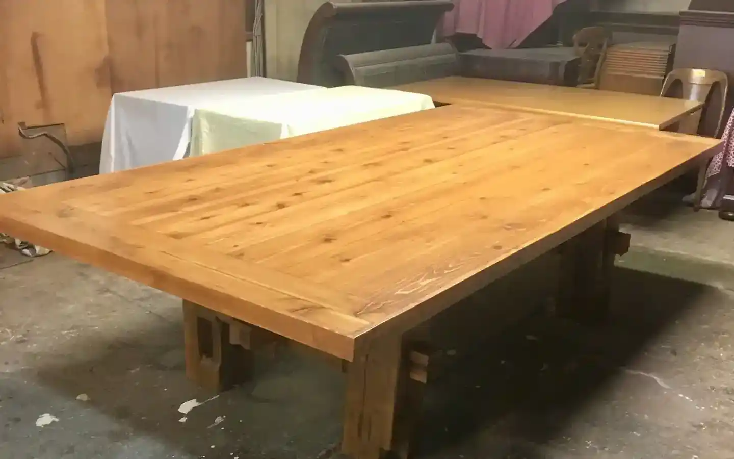 A long cedar plank table with trestle legs standing on the concrete shop floor