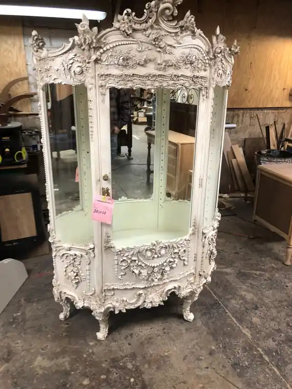 Ornate white painted vitrine with carved scrollwork and a curved glass front