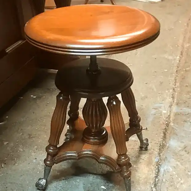 A round-topped wooden piano stool on fluted legs with clawed feet