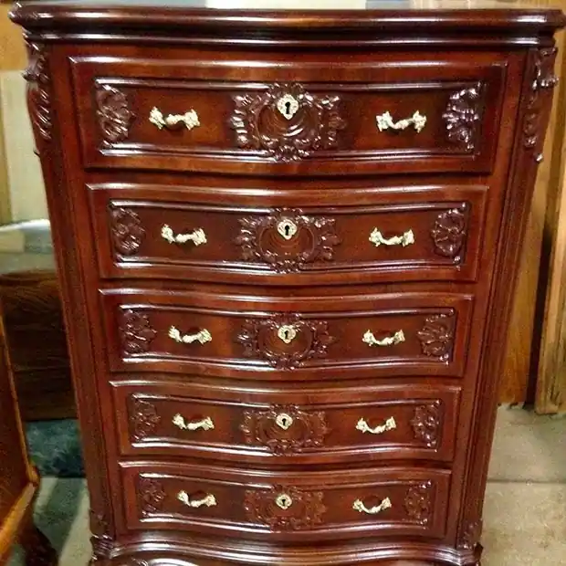 A tall serpentine chest with carved drawer fronts, brass keyhole escutcheons and brass bail pulls